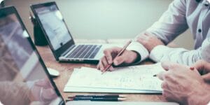 strategic career guide over a paper by one person wearing a shirt to the other in a desk setting with laptops and pens
