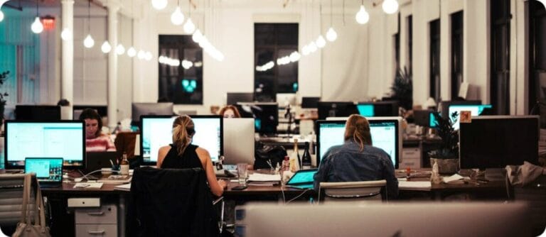 four people working looking at computer monitors in an office with full of lights