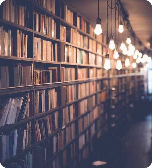 About 2 long bookshelf filled with books and bright light bulbs hanging on the ceiling