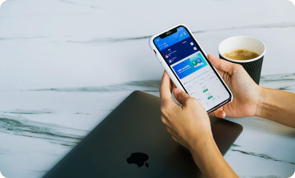 graphical user interface application on a cell phone next to a laptop and a cup of coffee