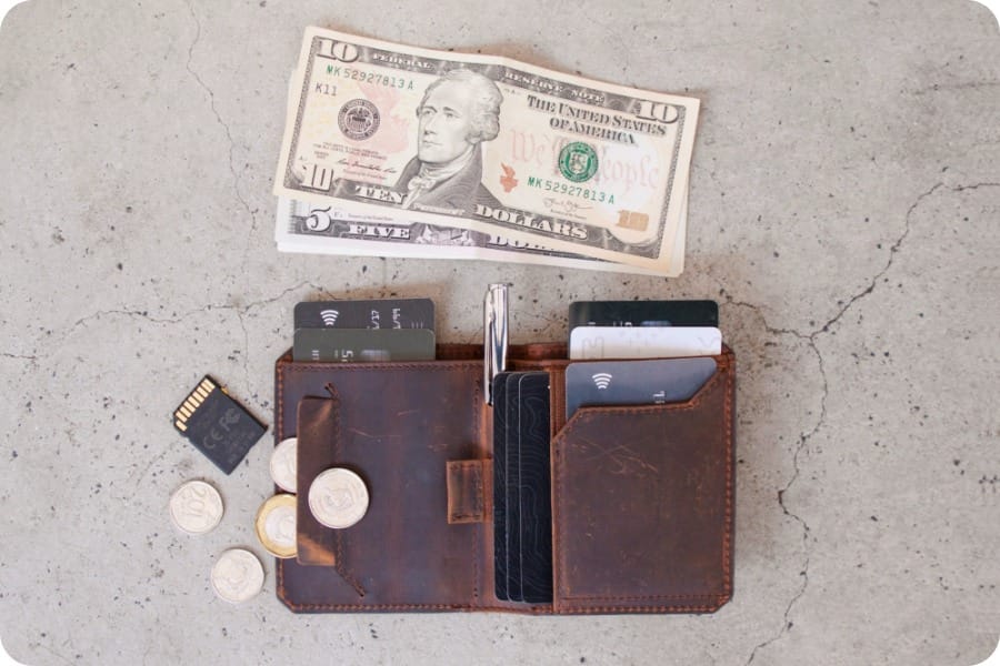 US bills and a brown leather wallet with credit cards and coins sticking out