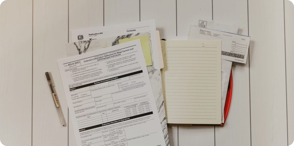 a stack of tax documents and note laying on a ground next to a pen