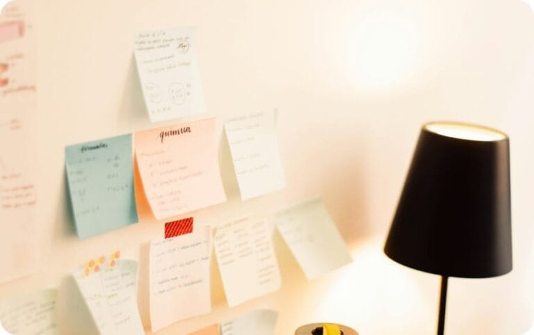 Blue, pink and white sticky notes on a white wall and a black stand light
