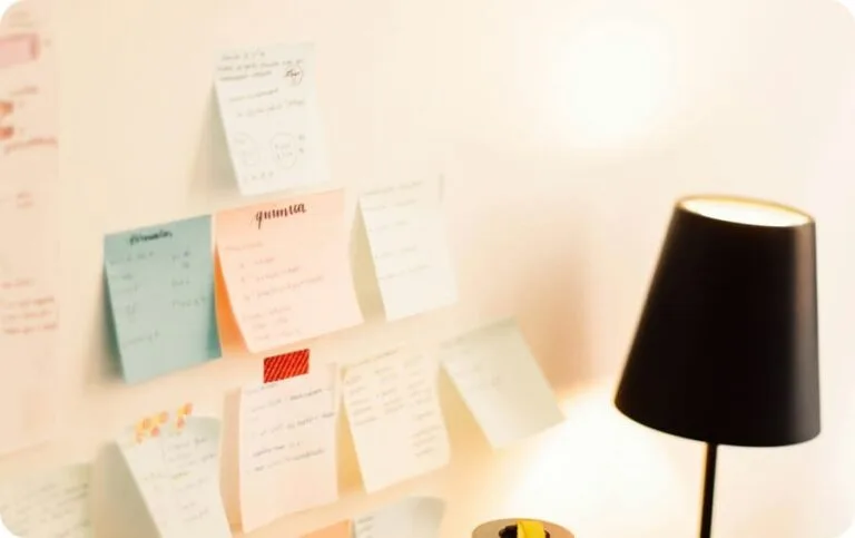 Blue, pink and white sticky notes on a white wall and a black stand light