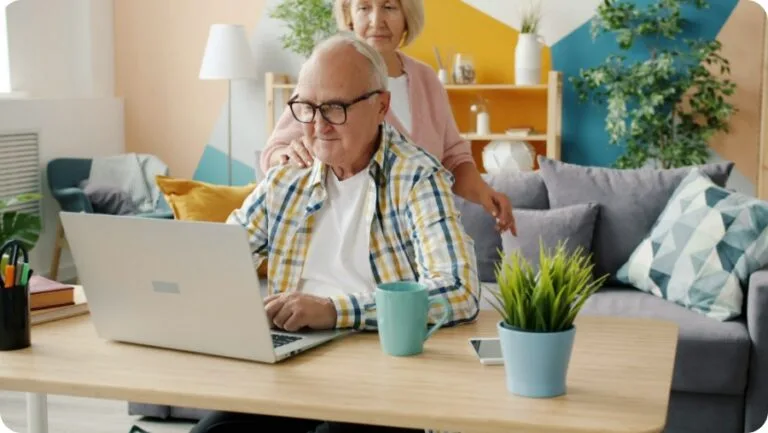 a senior man using laptop while his wife touching his shoulder looking at screen of the laptop