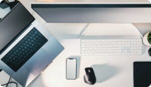 A computer, laptop, accessories and a cellphon on a white desk