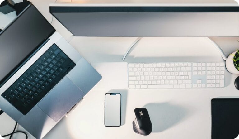 A computer, laptop, accessories and a cellphon on a white desk