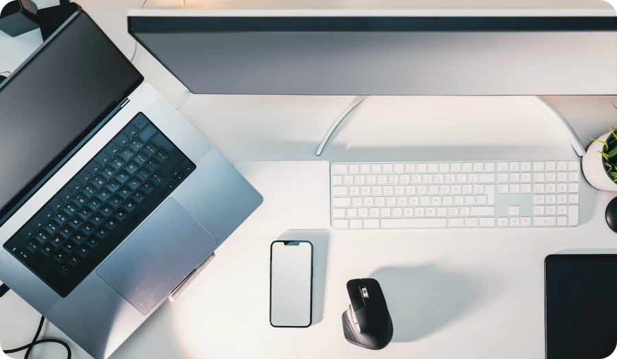 A computer, laptop, accessories and a cellphon on a white desk
